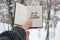 Hand holding a book with the inscription Say yes to new adventures on the background of the winter forest