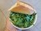 Hand holding a bowl of arugula greens and bread over tile floor