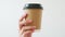 Hand holding a brown paper coffee cup and black cap on white background