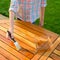 Hand holding a brush applying varnish paint on a wooden garden table