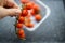 Hand holding a bunch of cherry tomatoes above a plastic container