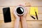 Hand holding coffee cup with smartphone and notepad on wood