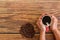 Hand holding a coffee mug on a wooden floor and a coffee bean beside it