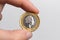 Hand holding a coin of one pound sterling with the image of Queen Elizabeth II close-up on a white background. UK currency