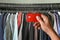 A hand holding credit card on t-shirts rack in shop