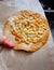 A hand holding a crunchy thin round shape biscuit topping with butter caramel peanut on light brown paper bag, pastry snack,