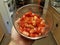 Hand holding cut red tomatoes in glass container in kitchen