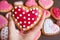 Hand holding a dotted heart shaped royal icing cookies with heap of blurry heart cookies in background