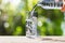 Hand holding drinking water bottle pouring water into glass on wooden tabletop on blurred green bokeh background with soft sunligh