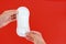 Hand holding feminine sanitary napkin, an absorbent item worn by a woman while menstruating, on red background