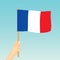 Hand holding France flag against blue sky