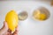 Hand holding a fresh lemon above a cup of lemon tea