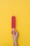 Hand holding a fresh strawberry popsicle on yellow background