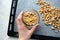 Hand holding glass jar with granola on parchment paper on baking sheet, top view. Made homemade healthy food