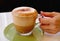 Hand holding a glass of mouthwatering frothy cappuccino coffee