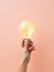 Hand holding a glowing lightbulb against a minimal backdrop, symbolizing the concept of innovative thinking and creativity.