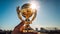 Hand holding golden trophy under the sunlight with blue sky background