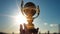 Hand holding golden trophy under the sunlight with blue sky background