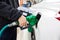 Hand holding a green filling gun while filling the fuel to a white car