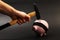 A hand holding a hammer which is raised above a upside down pink piggy bank with black blindfold standing on black background