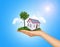 Hand holding house on green grass with tree, solar