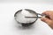 Hand holding ice tweezer with dry ice over black bowl of smoky white in motion  on white