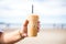 hand holding iced chai latte, with a blurred beach background