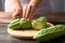 Hand holding knife and cutting bitter melon or bitter gourd