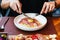 Hand holding knife and fork for eating Fettuccine Carbonara with parma ham and yolk with black pepper. Served in white plate