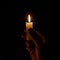 A hand holding a lighted candle in the dark. The light of a burning candle in a dark room. A candle on a black background