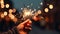 Hand holding a lit sparkler at night, with a warm glow and sparkling bokeh lights creating a festive and joyful atmosphere