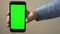 Hand holding mobile phone with green screen.