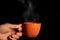 Hand holding mug with steam close up on black isolated background