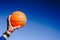 Hand holding an orange basketball ball on blue sky background, invitation to play, copy space free area