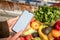 hand holding phone with white screen copy space in grocery shopping cart with fruits and vegetables