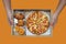 Hand holding pizza, fish rings and grilled chicken wings in paper box isolated on orange background.