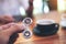 A hand holding and playing metal silver color fidget spinner with coffee cups and people using mobile phone