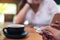 A hand holding and playing metal silver color fidget spinner with coffee cups and people using mobile phone