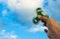 Hand holding popular green fidget spinner on sky background with copy space.