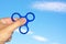 Hand holding popular green fidget spinner toy on sky background.