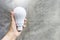 Hand holding portable rechargeable LED light bulb with space on grey cement wall background