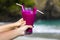 Hand holding purple cocktail in glass decorated with plastic straws  and piece of dragon fruit on the sandy tropical beach