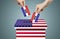 Hand holding and putting voting paper in ballot voting box with USA flag symbol.