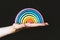 A Hand Holding A Rainbow. A beautiful, multi-colored, wooden rainbow in a woman`s hand on a black background. A symbol of happines
