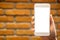 Hand holding and raising white mobile phone with blank desktop screen with brick wall background