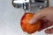 A hand is holding a red apple under the tap. Wash the apple