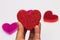 Hand holding a red Glitter heart against blurred hearts on white background