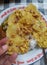 Hand holding Rempeyek or Peyek Kacang, Indonesian traditional savoury peanut crackers with plate of rice as blurred background.