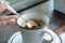 A hand holding silver spoon scooping some hot black coffee from a white ceramic mug