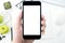 Hand is holding a smartphone with blank mockup screen above the white desk table